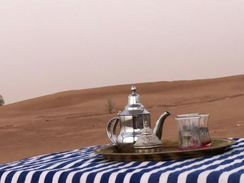 a tea pot and glasses on a table in the desert at Sahara Authentic Berber Camp in Mhamid