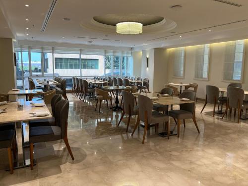 Gloria Hotel & Suites Doha في الدوحة: مطعم بطاولات وكراسي في غرفة بها نوافذ