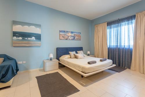 Dormitorio azul con cama y ventana en Waters-Edge Complex, en Marsaskala