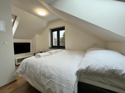 a bedroom with a large white bed and a television at PLESSBERG Apartments Plešivec in Abertamy