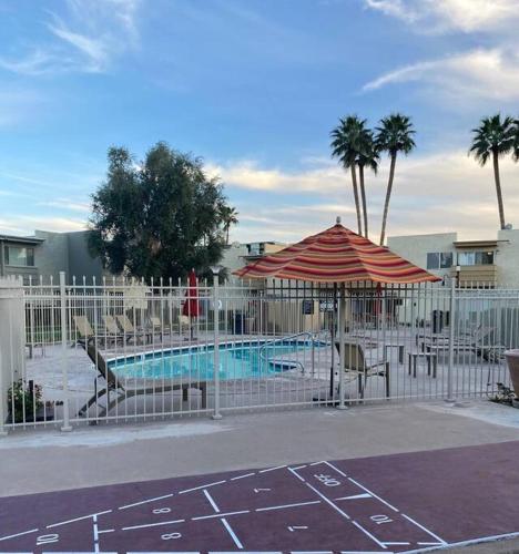 a pool with an umbrella and chairs next to a fence at Entire 2 level townhouse in Old Town Scottsdale! in Scottsdale