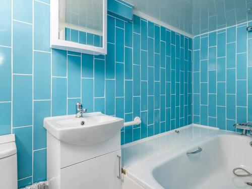 une salle de bain bleue avec un lavabo et une baignoire dans l'établissement "FurnishedRentals Direct" WiggenHouse Stylish 3 Bedroom house Sleeps 8 with Free Parking, 2 Bathrooms, near to Watford High Street and Watford Football Stadium, Suitable for visiting Harry Potter Warner Bros Studio and London, à Watford