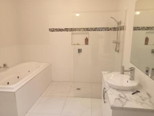 ein weißes Badezimmer mit einer Badewanne und einem Waschbecken in der Unterkunft Luxurious entire family home in Mooroopna