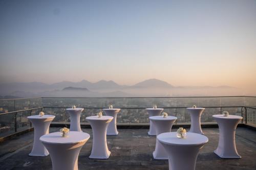 a row of white tables on a balcony with mountains in the background at Crowne Plaza Vinh Yen City Centre by IHG in Yen