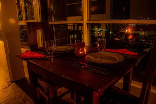 a wooden table with plates and glasses and a window at MANUDI Glenfallsedge Rest in Nuwara Eliya