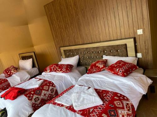 three beds in a hotel room with red and white pillows at Bronze Mountains Camp Wadi Rum in Aqaba
