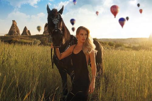 a woman holding a horse in a field with hot air balloons at Mak's Cave House in Uchisar
