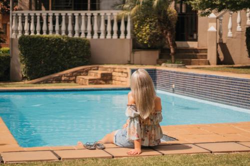 a young girl sitting next to a swimming pool at All Seasons Boutique Hotel in Pretoria