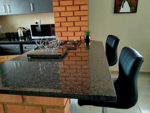 a dining table with black chairs and a brick wall at Modern 2 bedroom at Waterfall Ridge-Midrand in Midrand