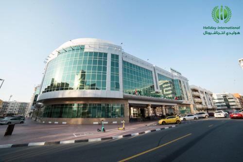 Holiday International Hotel Embassy District في دبي: مبنى زجاجي كبير فيه سيارات تقف امامه