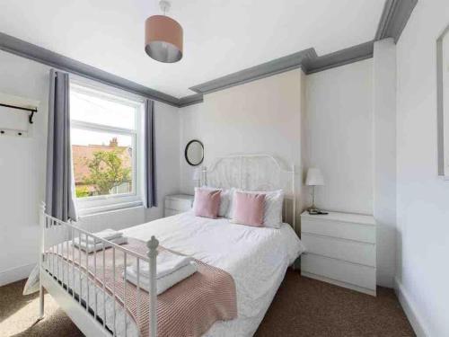 a bedroom with a white bed with pink pillows and a window at West Lodge, Filey. Sleeps 8, 7 mins walk to beach in Filey