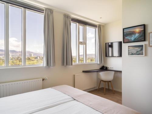 a bedroom with a bed and a desk and windows at Reykjavik Lights Hotel by Keahotels in Reykjavík
