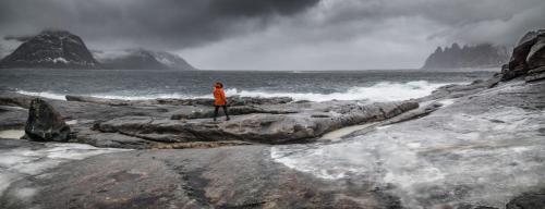 Eine Person, die auf Felsen in der Nähe des Ozeans steht in der Unterkunft Skagi Senja hotel & lodge in Skaland