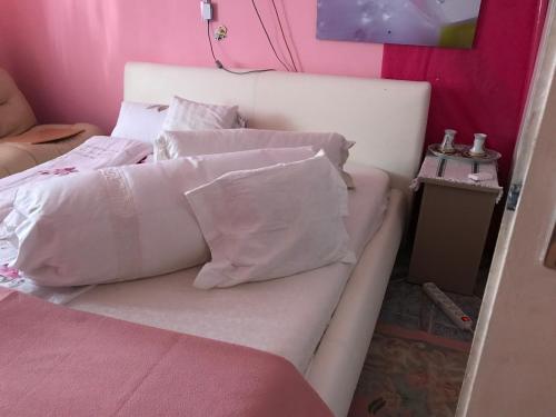 1 cama blanca con almohadas blancas y pared rosa en Külön apartman fiatal pároknak hosszútávra feléért!, en Budaörs