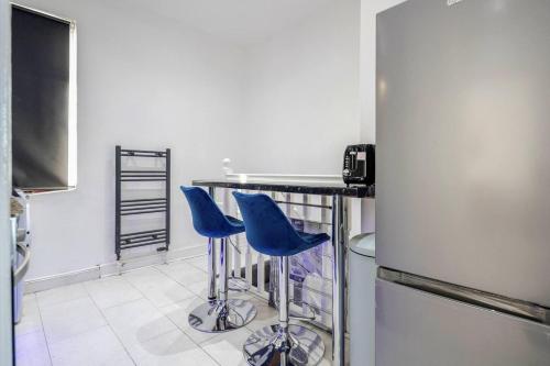 a kitchen with two blue bar stools and a refrigerator at Stunning Top 2 Bed Flat Tilbury Central Location in Tilbury