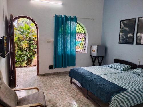 a bedroom with a bed and a window and a chair at Rosetta Guesthouse in Anjuna