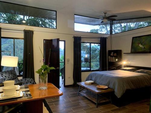 1 dormitorio con cama, mesa y algunas ventanas en Modern cabin nestled in mountain nature. Paradise! en Orosí
