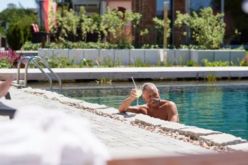 a man in a swimming pool with a straw at Landhotel Haringerhof mit Saunawelt und Naturbadeteich in Grafenhausen