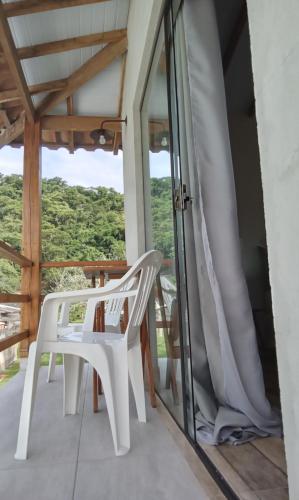 a room with a balcony with white chairs and windows at Suíte Ilhinha II em condomínio na Praia do Perequê in Ilhabela