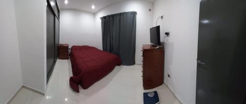 Habitación pequeña con cama roja y TV. en Dpto estrada en Ezeiza