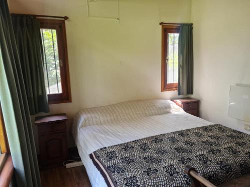 a small bedroom with a bed and two windows at Cabaña en los Acantilados in Mar del Plata