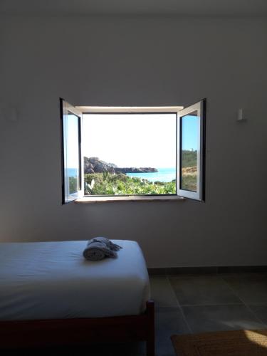 ein Schlafzimmer mit einem Bett und einem offenen Fenster in der Unterkunft Tasi Ingrina in Vila do Bispo