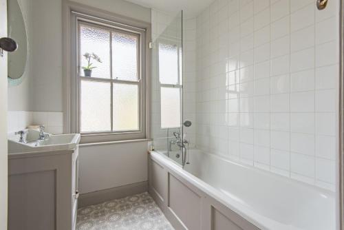 La salle de bains blanche est pourvue d'une baignoire et d'un lavabo. dans l'établissement Prospect Cottage by Bloom Stays, à Hythe