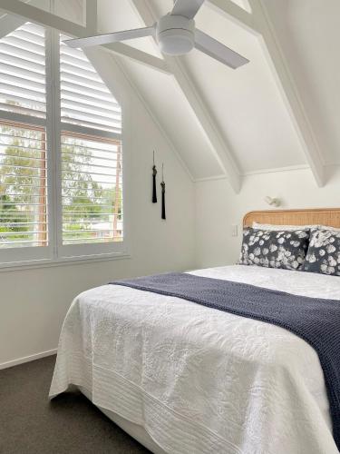 a bedroom with a white bed with a ceiling fan at The Loft Matua in Tauranga