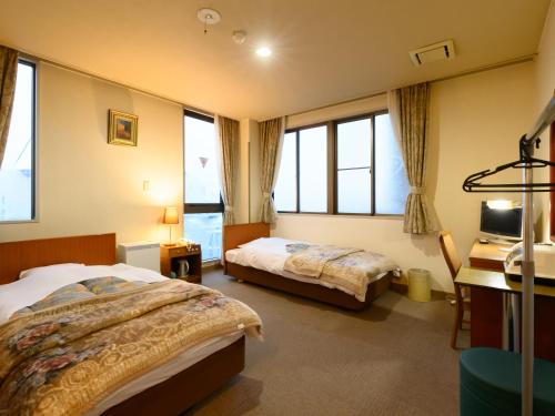 a bedroom with two beds and a desk and windows at Business Ryokan Hotel Yukimiso in Toyama