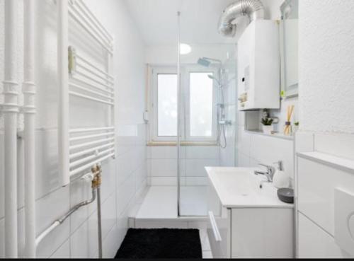La salle de bains blanche est pourvue d'une douche et d'un lavabo. dans l'établissement Schickes Appartement an der Neckarpromenade, à Heilbronn