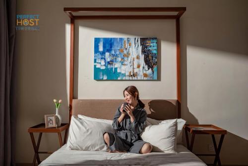 Timurbay Beachfront by Perfect Host في كُوانتان: امرأة جالسة على سرير تتحدث على الهاتف الخلوي