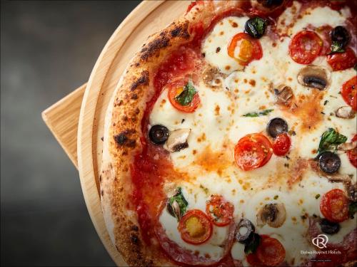 a pizza with tomatoes and olives on a wooden plate at Daiwa Roynet Hotel Kanazawa Eki Nishiguchi in Kanazawa