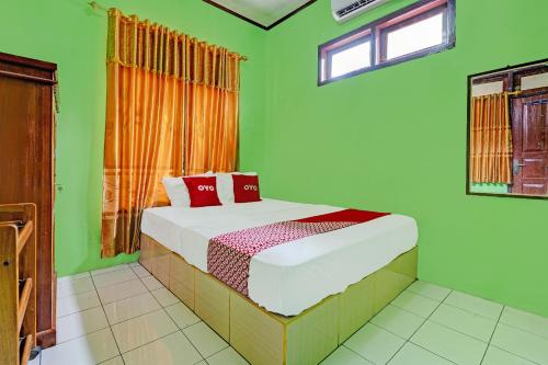 ein grünes Schlafzimmer mit einem Bett mit roten Kissen in der Unterkunft OYO 92062 Pondok Aurel Wahidin in Cirebon