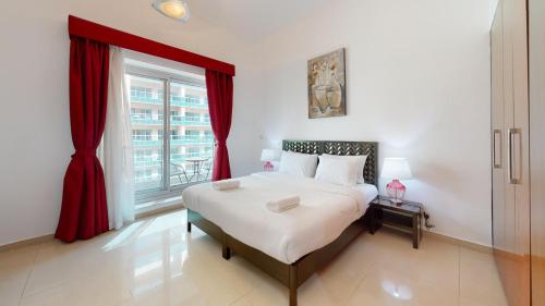 a bedroom with a bed with red curtains and a window at Hometown Apartments - Waterfront 1 Bedroom apartment in Westside Marina in Dubai