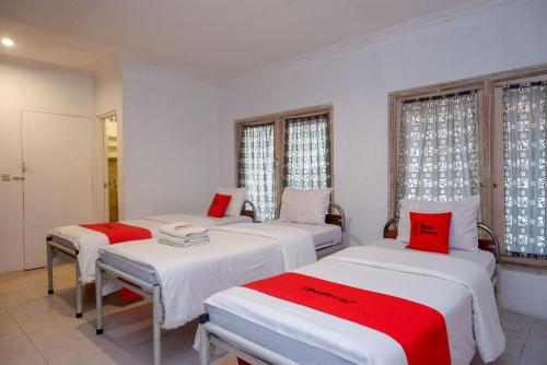 Habitación con 3 camas con sábanas rojas y blancas. en RedDoorz Syariah near Plengkung Gading 2 en Yogyakarta