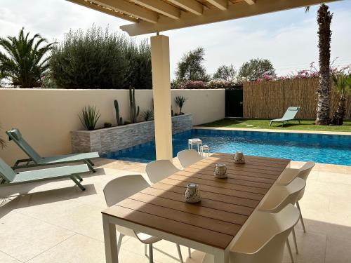a patio with a wooden table and chairs next to a pool at Villa Nawal et sa piscine chauffée sans vis-à-vis in Agadir