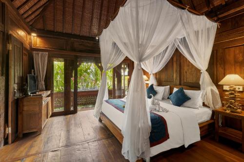 ein Schlafzimmer mit einem Bett mit Moskitonetz in der Unterkunft Kawan Antique Ubud Villa in Ubud