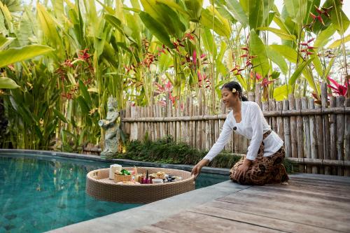 eine Frau, die auf dem Boden neben einem Swimmingpool sitzt in der Unterkunft Kawan Antique Ubud Villa in Ubud