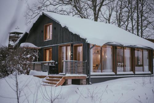 eine grüne Hütte im Schnee mit einem schneebedeckten Dach in der Unterkunft VIESU MĀJA KALNARUŠĶI in Lūšakrogs