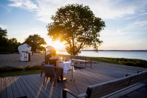 a couple sitting at a table on a deck near the water at Aedenlife Hotel & Resort Rügen in Trent