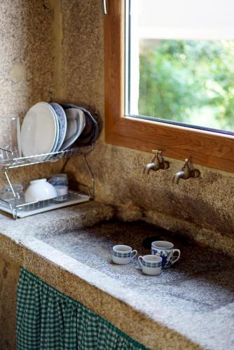 a kitchen counter with cups and plates and a window at Casa de Chica Ecoturismo in Lousame