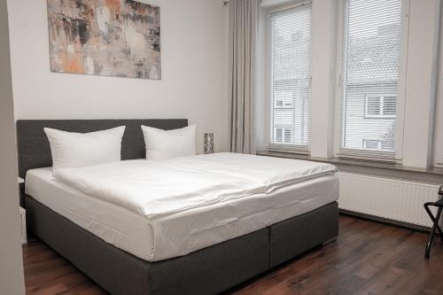 a bedroom with a bed with white sheets and two windows at Hotel Teatro in Kassel