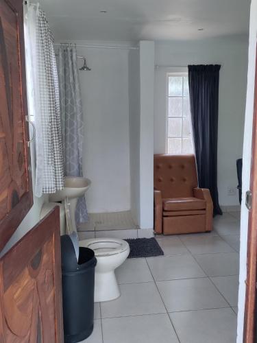 uma casa de banho com um WC, uma cadeira e uma janela. em Outside room em Pretoria