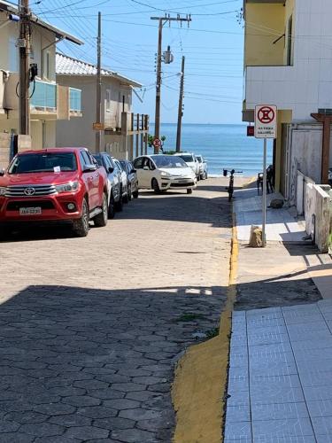 ulica z samochodami zaparkowanymi obok oceanu w obiekcie Apartamento itapirubá w mieście Imbituba