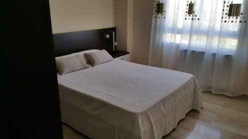 een slaapkamer met een bed met witte lakens en een raam bij GRANJA-CLIMATIZADO-Parking gratis in Jaén