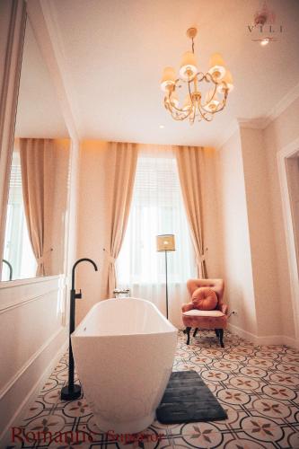 a bathroom with a tub and a chair and a chandelier at Vili Apartments in Oradea