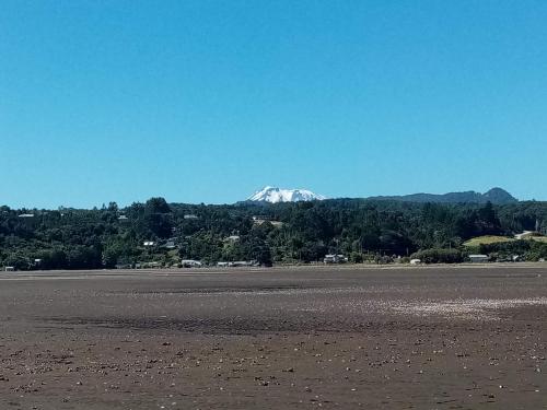 una montaña cubierta de nieve en la distancia detrás de una playa en Cycling Hostel Piedra Azul, en Puerto Montt