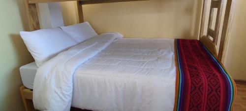 ein Bett mit weißer Bettwäsche und einer roten Decke in der Unterkunft cusco pasay in Cusco