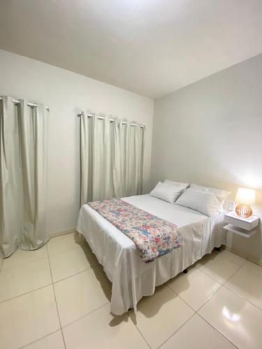 a white bedroom with a bed and a lamp on a table at FLATS VALLE DEL SOL in Japaratinga