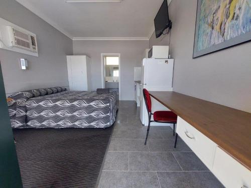 Kleines Zimmer mit einem Bett und einem Schreibtisch sowie einem Zimmer mit einem Kühlschrank. in der Unterkunft Collie Motel in Collie